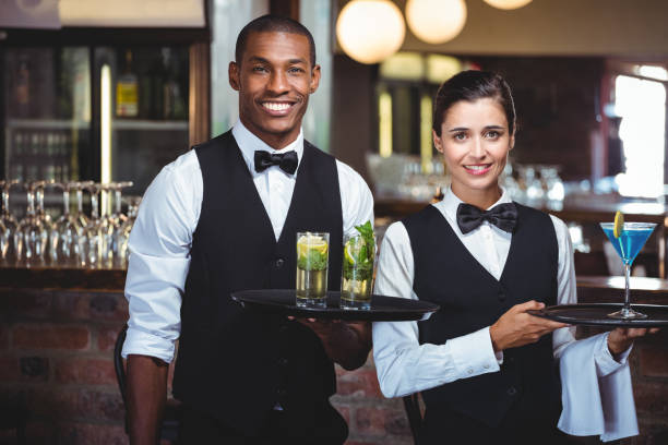 Portrait of waiter and waitress holding a serving tray with glass of cocktail UNIFORM COLLECTION6 - Image 1